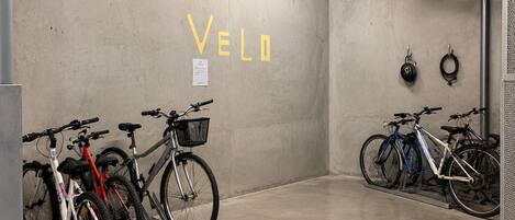 A bicycle parking area with the word 'VELO' on the wall, a bike rack, and a helmet hanging on the wall.