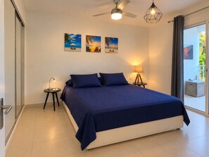 A bedroom with a bed, a ceiling fan, a nightstand with a lamp, and three wall-mounted pictures.