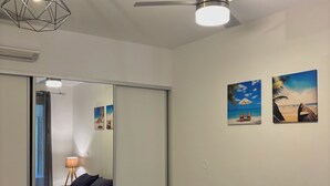 Una camera da letto con un letto, una ventola a soffitto, una lampada a parete e due dipinti a tema spiaggia.