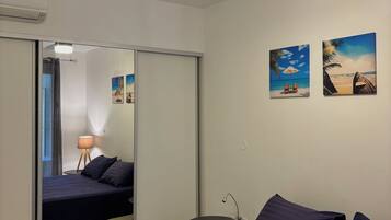 A bedroom with a bed, a ceiling fan, a wall-mounted lamp, and two beach-themed paintings.