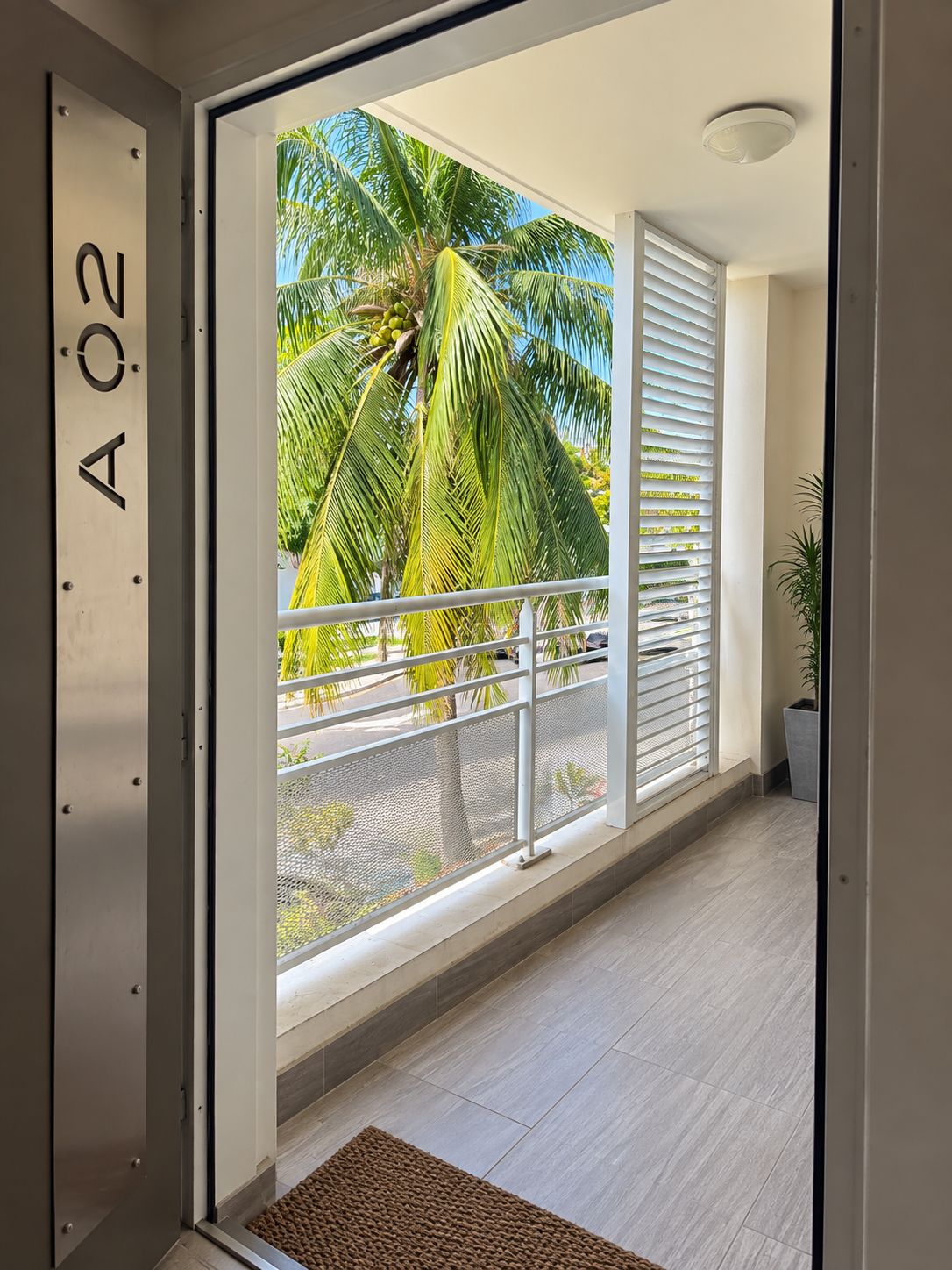A modern interior with a balcony overlooking palm trees and a clear sky.