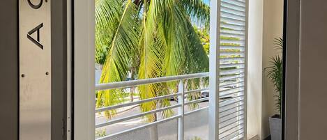 A modern interior with a balcony overlooking palm trees and a clear sky.