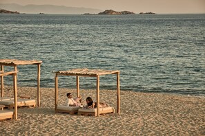 Ein Strand mit Holzkonstruktionen als Sonnenschutz, feinem Sand und einem ruhigen Meer mit entfernten Inseln.