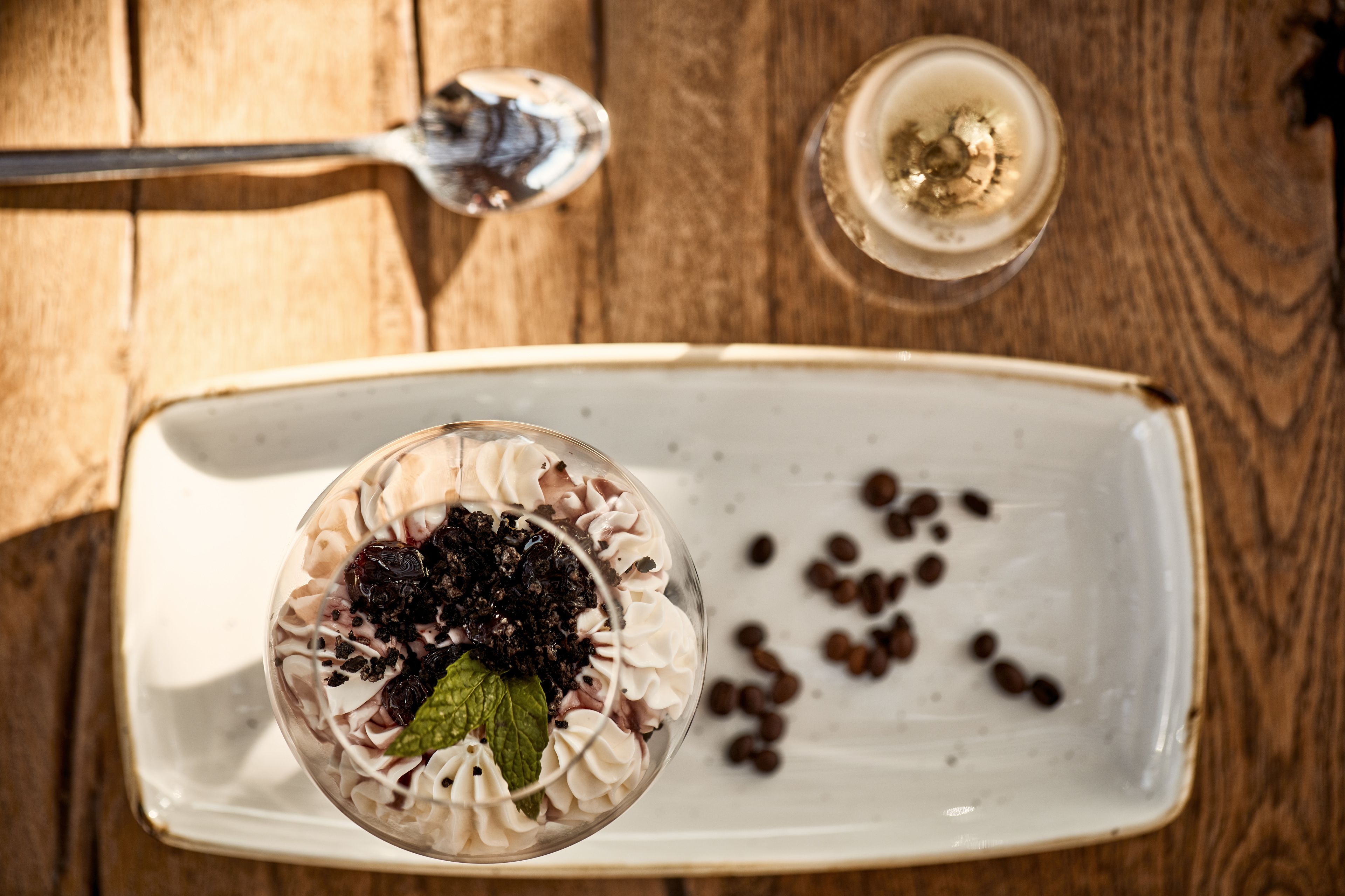 A dessert in a glass on a white plate with coffee beans scattered around.