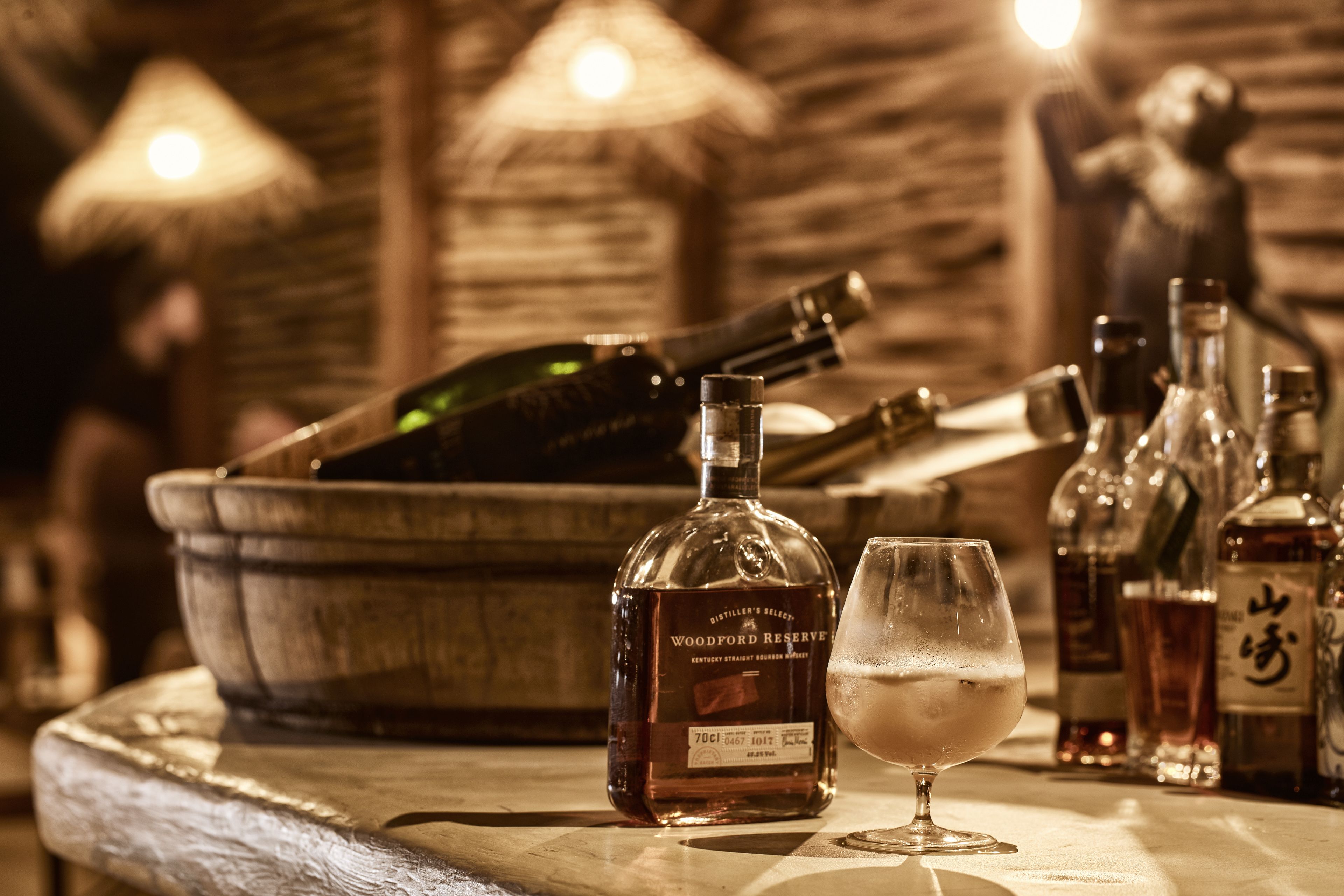 Un'atmosfera da bar con una bottiglia di Woodford Reserve, un bicchiere di whiskey e diverse bottiglie sullo sfondo.