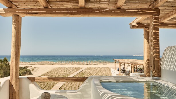 A wooden pergola overlooking a beach with a hot tub and seating area.