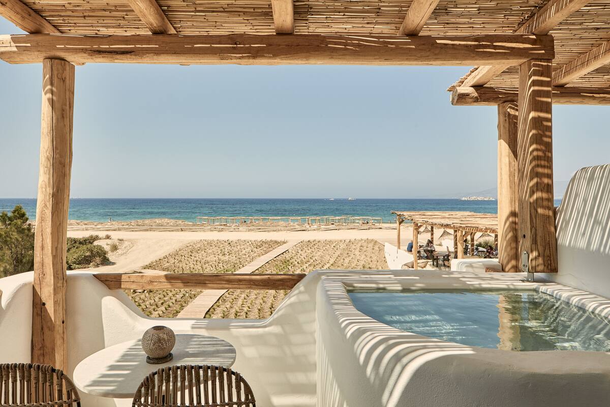 Une pergola en bois donnant sur une plage, avec un jacuzzi et un espace salon.