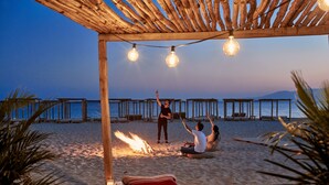A beach setting with a wooden pergola, string lights, and a fire pit.