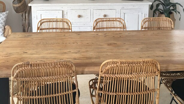 Un coin repas avec une table en bois et des chaises en osier, un meuble blanc agrémenté d’objets décoratifs et un luminaire suspendu en fibres tressées.