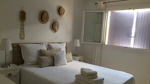 Une chambre à coucher bien rangée, avec un lit, des oreillers, une table de chevet, une lampe et une fenêtre avec des stores.