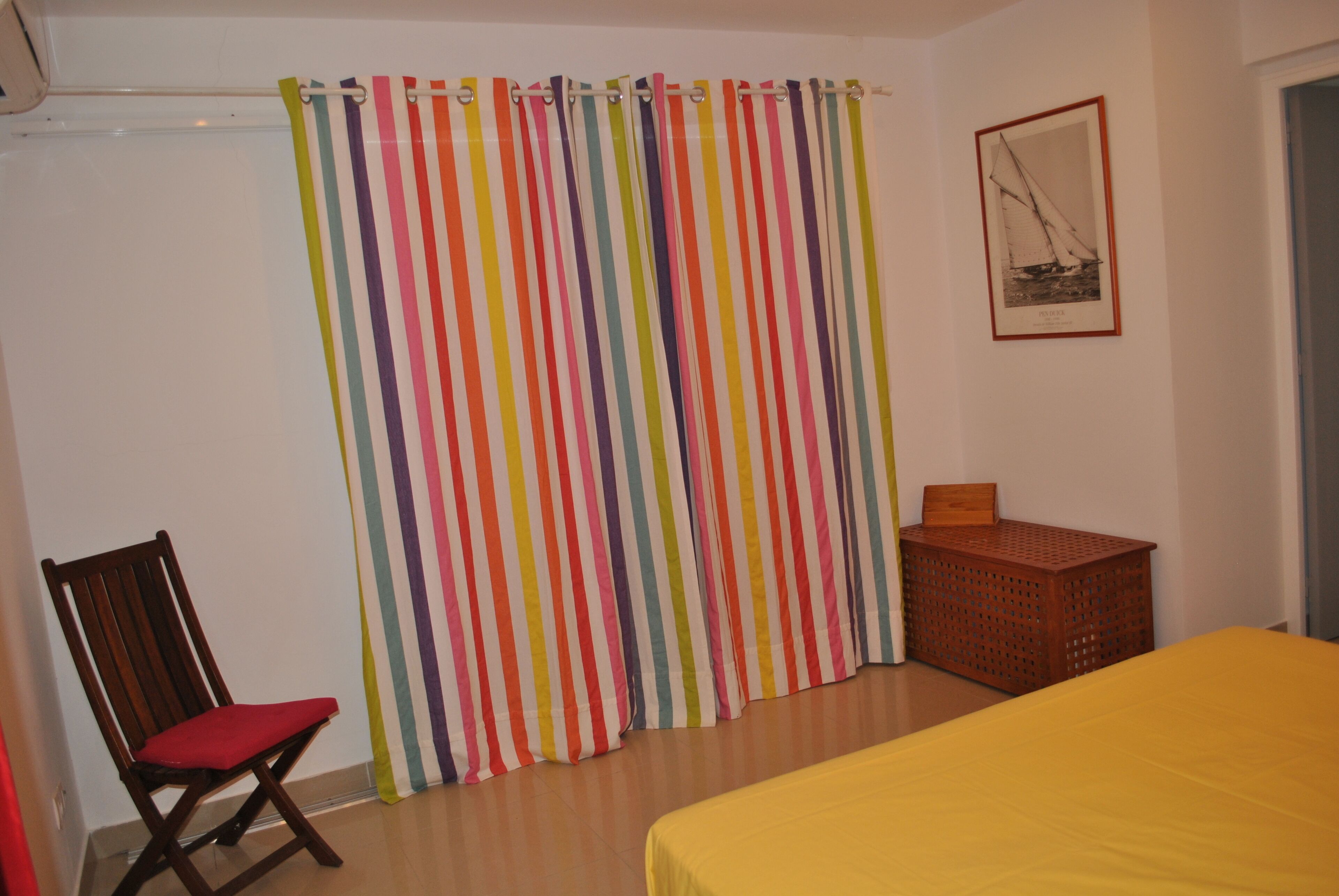 A bedroom with a bed, a chair, a colorful striped curtain, and a framed picture on the wall.