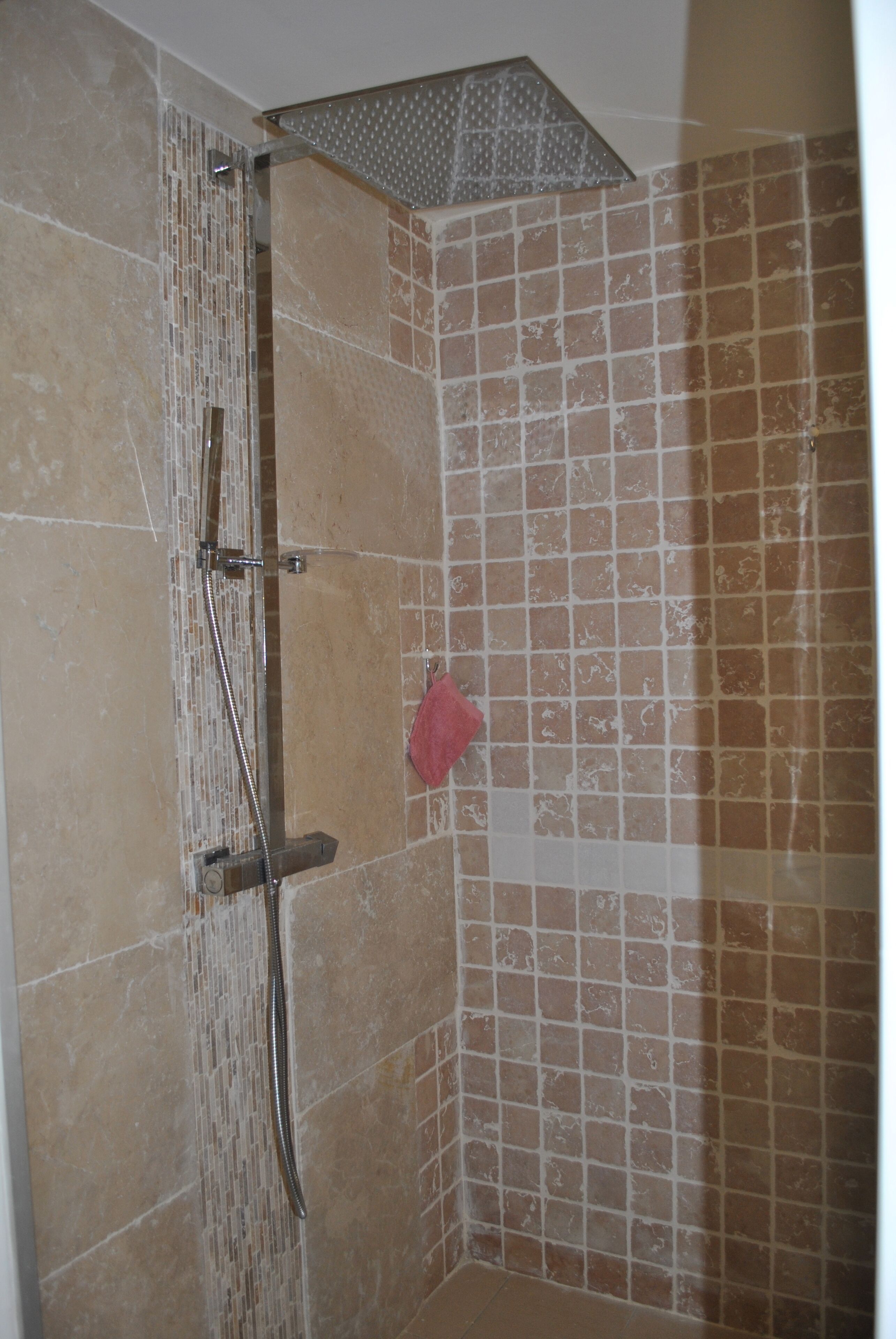 Chuveiro com chuveiro de teto e chuveiro manual, paredes azulejadas e uma toalha vermelha pendurada na parede.