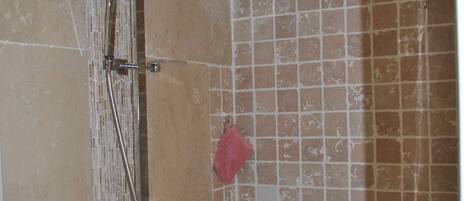 Chuveiro com chuveiro de teto e chuveiro manual, paredes azulejadas e uma toalha vermelha pendurada na parede.