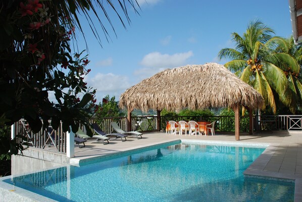 A swimming pool with lounge chairs and a thatched-roof structure. - 76m2 apartment on one level, large infinity pool, sea view, garden (Le Robert)
