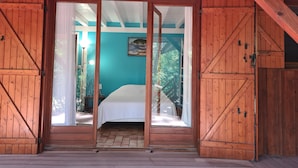 A wooden cabin with a large sliding door leading to a bedroom with a bed and a painting on the wall.