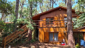 A wooden cabin with a staircase leading to a second level, surrounded by trees.