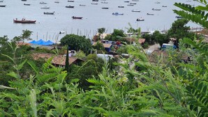 A coastal view with numerous boats on the water, a small settlement with houses and a blue tent, and lush greenery in the foreground.
