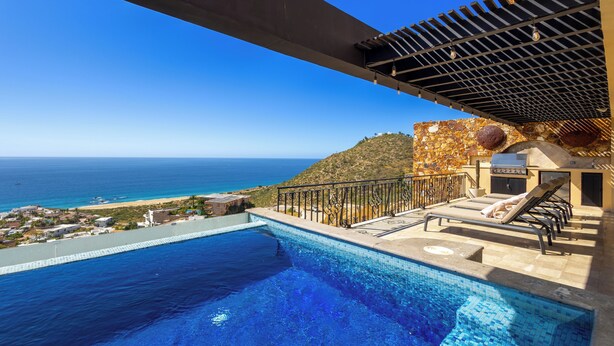 A rooftop infinity pool with a view of the ocean, a pergola, and a lounge area with sun loungers.