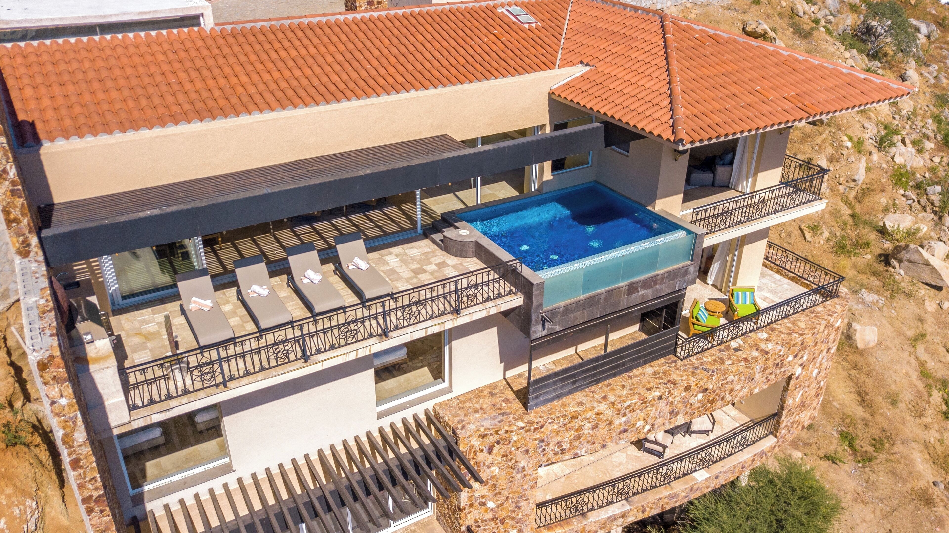 Une maison moderne à deux étages, dotée d’une piscine sur le toit, d’un espace extérieur aménagé et d’une façade en pierre.