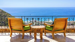 A wooden bench and table with green cushions on a balcony overlooking the ocean.