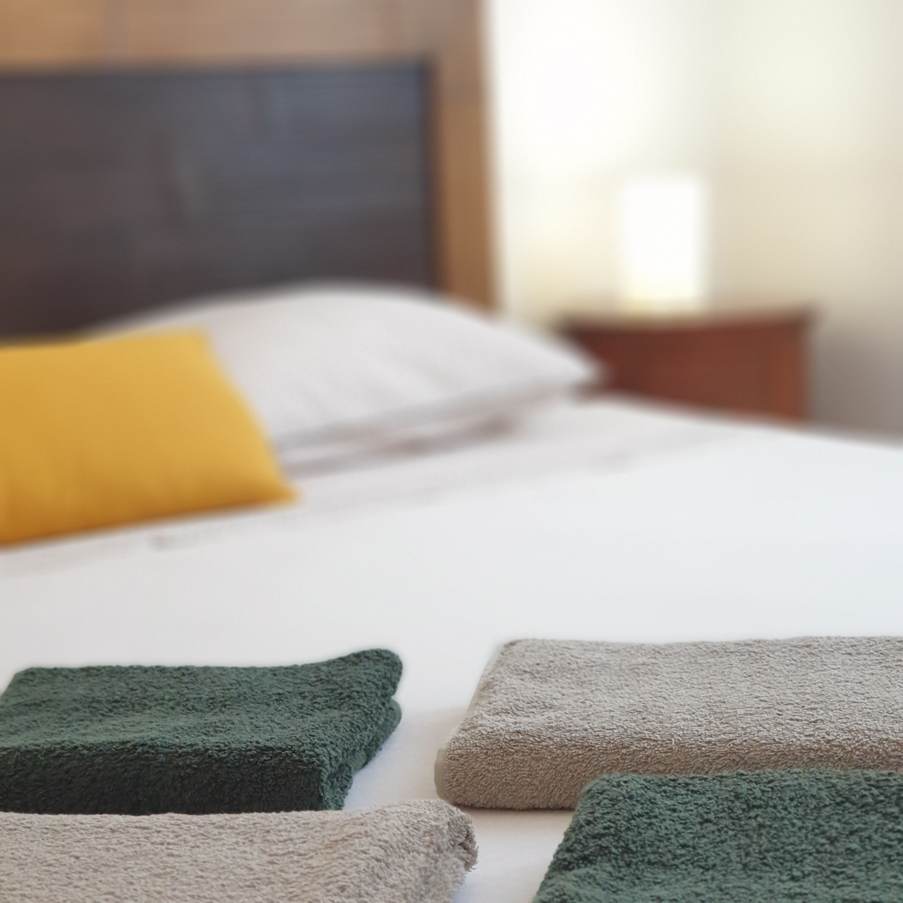Una cama bien hecha con sábanas blancas y varios almohadones, incluyendo uno amarillo.