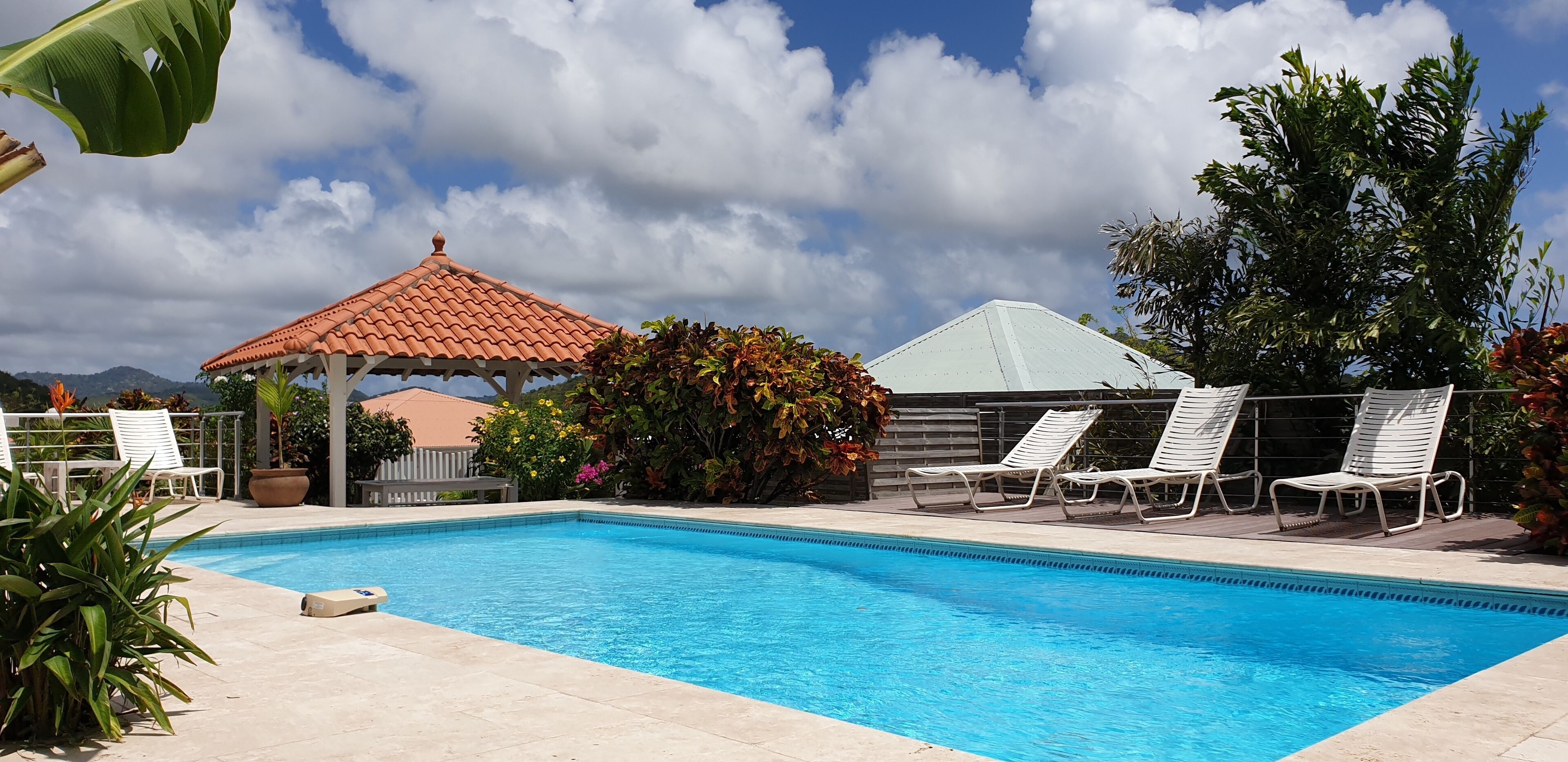 A swimming pool with lounge chairs, a gazebo, and lush greenery.
