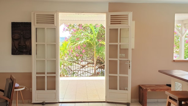Een kamer met een grote openslaande deur die leidt naar een balkon met uitzicht op een tuin en een houten hek.