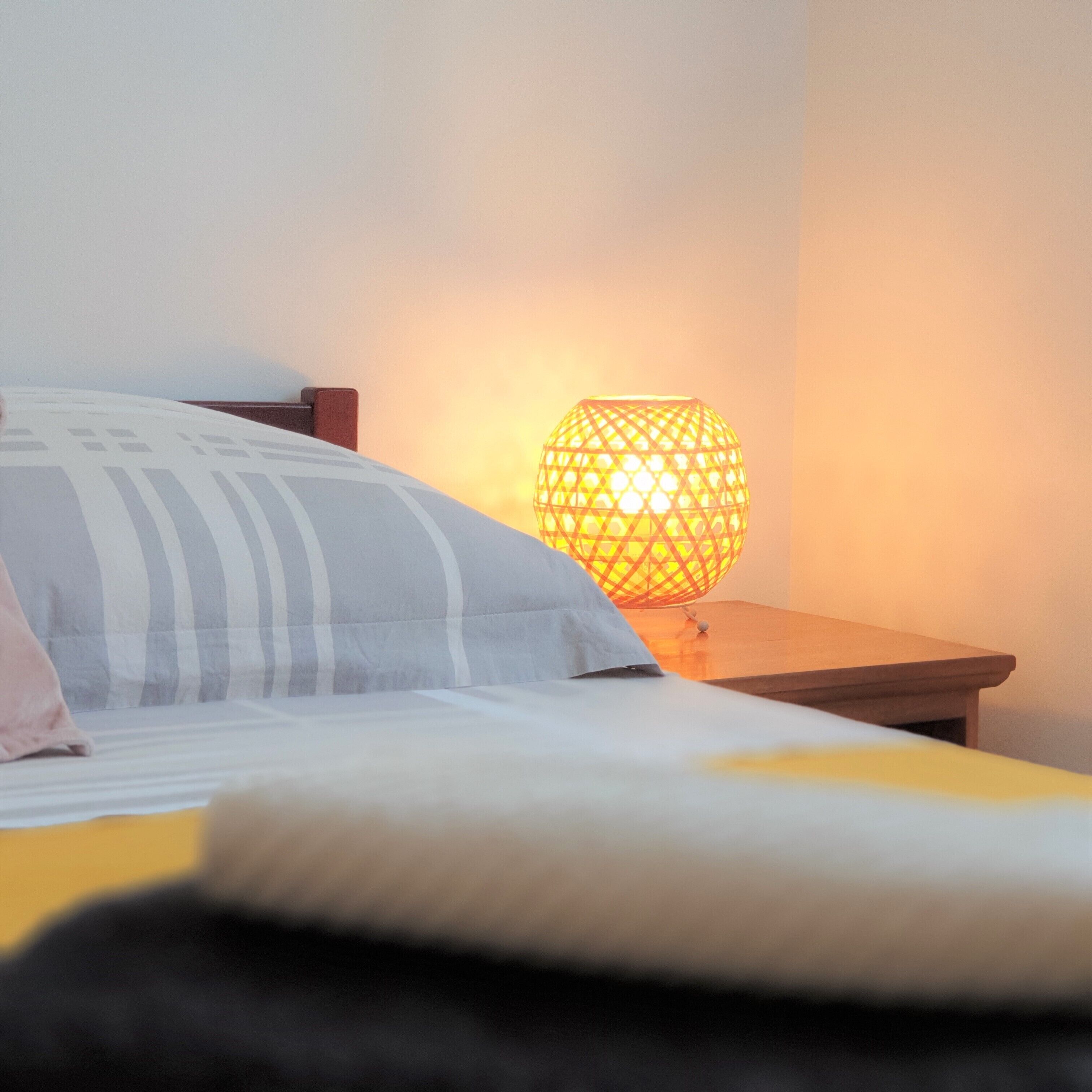 Een bed met een gestreept kussen en een nachtkastje van hout met een bolvormige lamp.