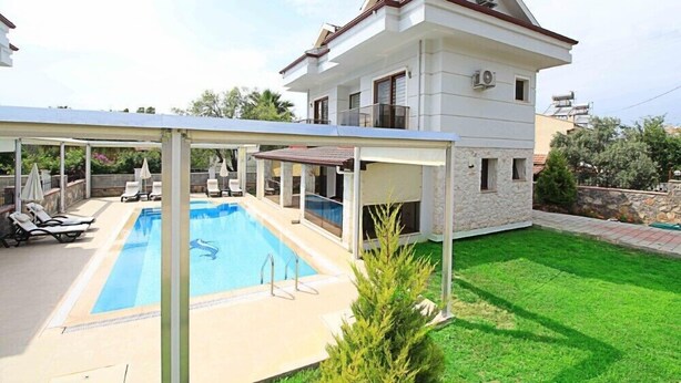 Una casa de dos pisos con piscina, terraza cubierta y césped bien cuidado.