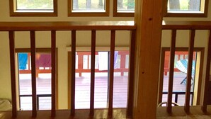 Une pièce dotée de grandes fenêtres, de poutres en bois et offrant une vue sur une terrasse et les arbres à l’extérieur.