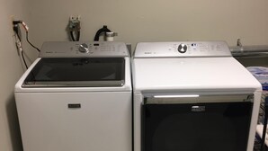 Two Maytag front-loading washers in a laundry room with a tiled floor and a metal rack in the background. - Beautiful Large Loft on Historic Water Street in Downtown Decorah (Decorah)