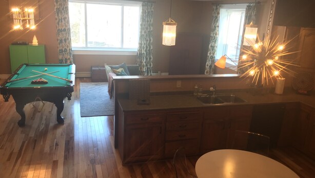 A living room with a pool table, a dining table, and a kitchen area. - Beautiful Large Loft on Historic Water Street in Downtown Decorah (Decorah)