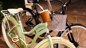 Una bicicleta antiga amb un cistell i un suports marró per a tassa, aparcada sobre una superfície de rajola.