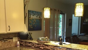 Cuina amb encimera de granit, armaris blancs i il·luminació penjant.