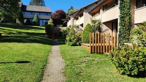 A pathway leading to a building with a traditional architectural style, surrounded by well-maintained greenery and a clear blue sky. - VALLEY RIO cottage style 2/6 persons (Le Chambon-Sur-Lignon)