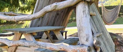 Ein Holztisch für ein Picknick mit einer Hängematte und einer Holzkonstruktion, die einem Vogelhaus oder einer Laube ähnelt.