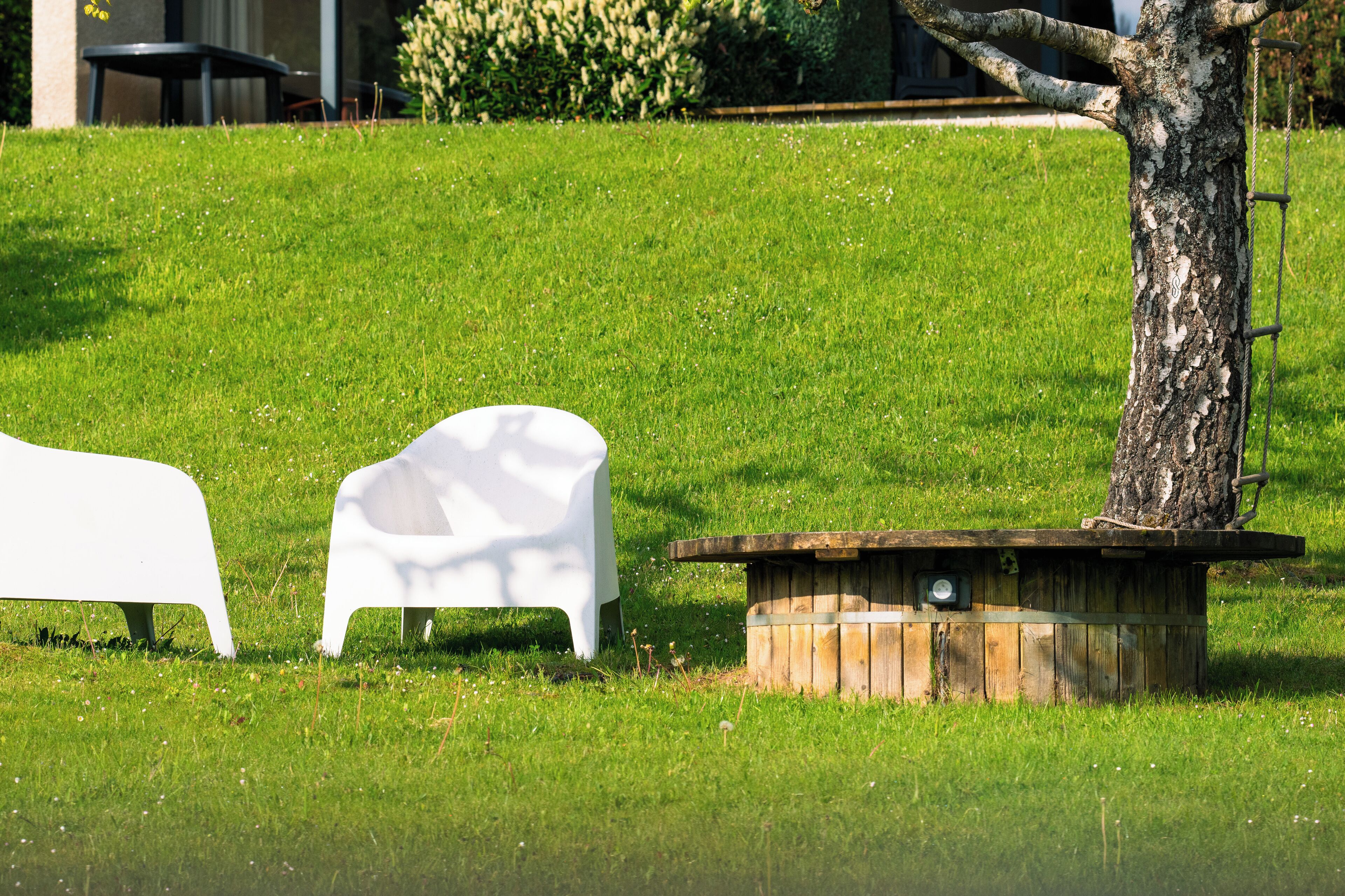 A grassy outdoor area with a wooden bench and a white chair.