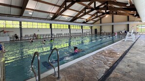 En indendørs swimmingpool med tydelige baner, en redningsbøje og et højt loft med træbjælker.
