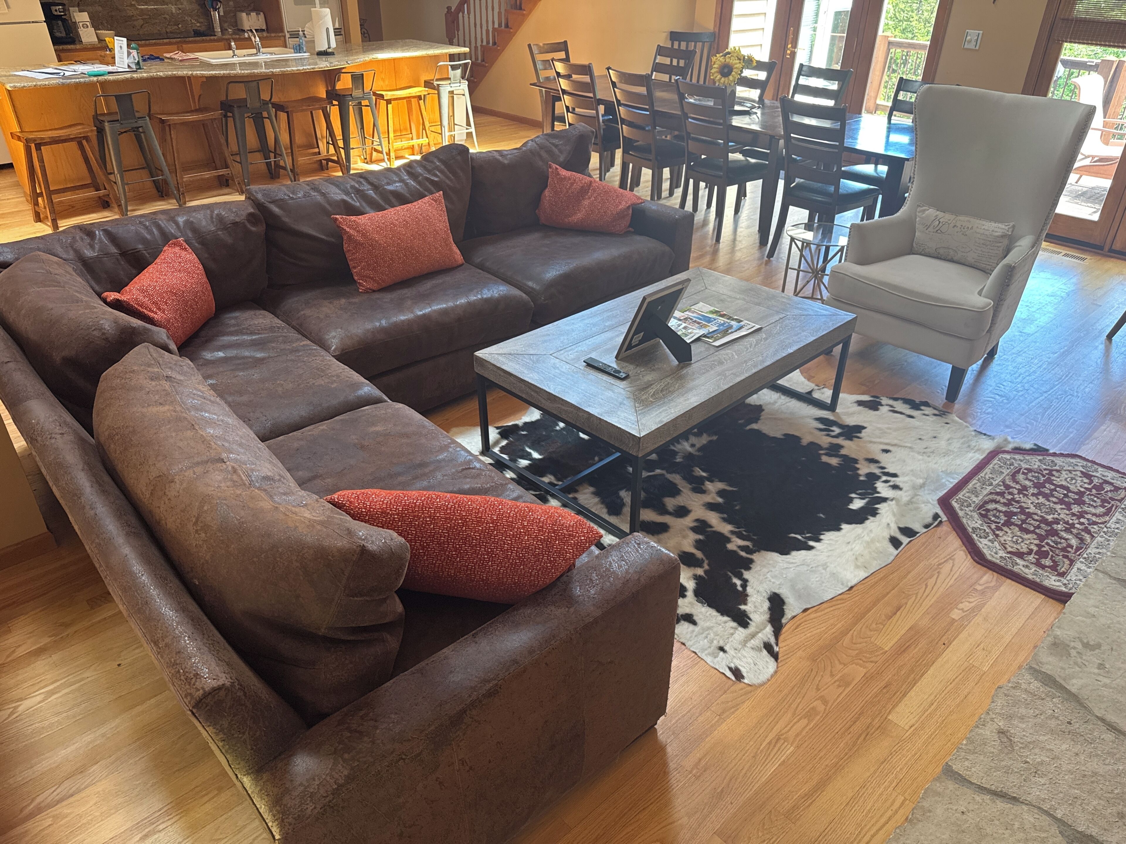 A living room with a sectional sofa, a coffee table, a cowhide rug, and a dining area with chairs and a table.