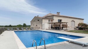 A two-story stone house with a swimming pool, outdoor seating, and a covered patio.