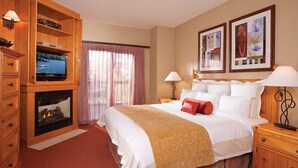 A hotel room with a bed, a television on a wooden cabinet, a fireplace, and artwork on the walls.
