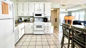 Una cocina compacta con gabinetes blancos, un microondas, un horno y una cafetera.