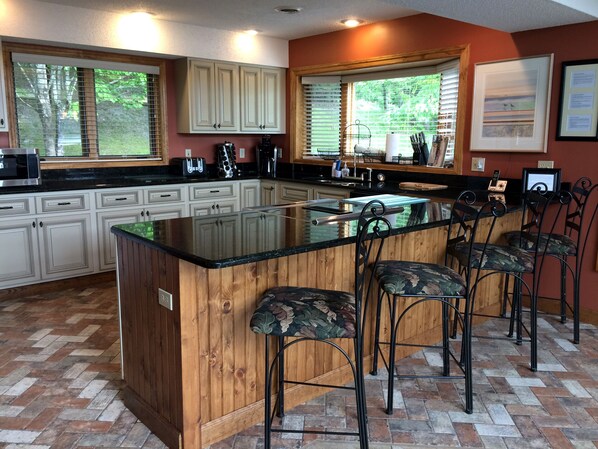 Une cuisine dotée d’un grand îlot central, de tabourets de bar, de meubles en bois et d’un parquet disposé en motif à chevrons.
