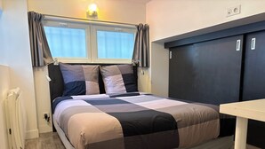 Ein modernes Schlafzimmer mit einem Bett, einem Nachttisch, einem Fenster mit Vorhängen und einer Wandleuchte.