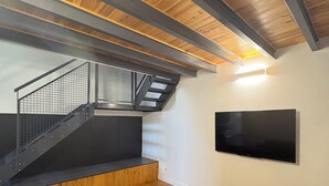 Ein modernes Wohnzimmer mit Holzboden, einem grauen Sofa, einem an der Wand montierten Fernseher und einer Treppe mit Metallgeländer.