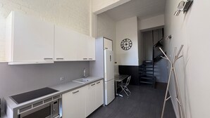 Eine moderne Küche mit weißen Schränken, einem Einbauofen und einem Kühlschrank. Es gibt einen Essbereich mit Tisch und Stühlen sowie eine Treppe zu einer anderen Ebene.