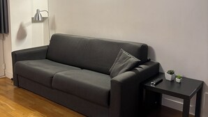 Ein modernes Wohnzimmer mit einem dunkelgrauen Sofa, einem kleinen schwarzen Beistelltisch mit einer Fernbedienung und einem Blumentopf.
