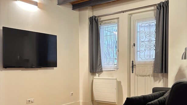 Ein modernes Wohnzimmer mit einem an der Wand montierten Flachbildfernseher, einem schwarzen Sofa, einem Couchtisch mit Pflanzen und Holzboden.