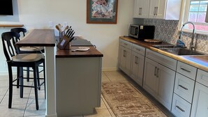 Une cuisine avec un îlot central, des chaises foncées, un four à micro-ondes et un tapis à motifs.