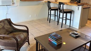 Un salon comprenant une table basse, deux fauteuils, un téléviseur fixé au mur et un coin cuisine avec un four à micro-ondes et des placards.
